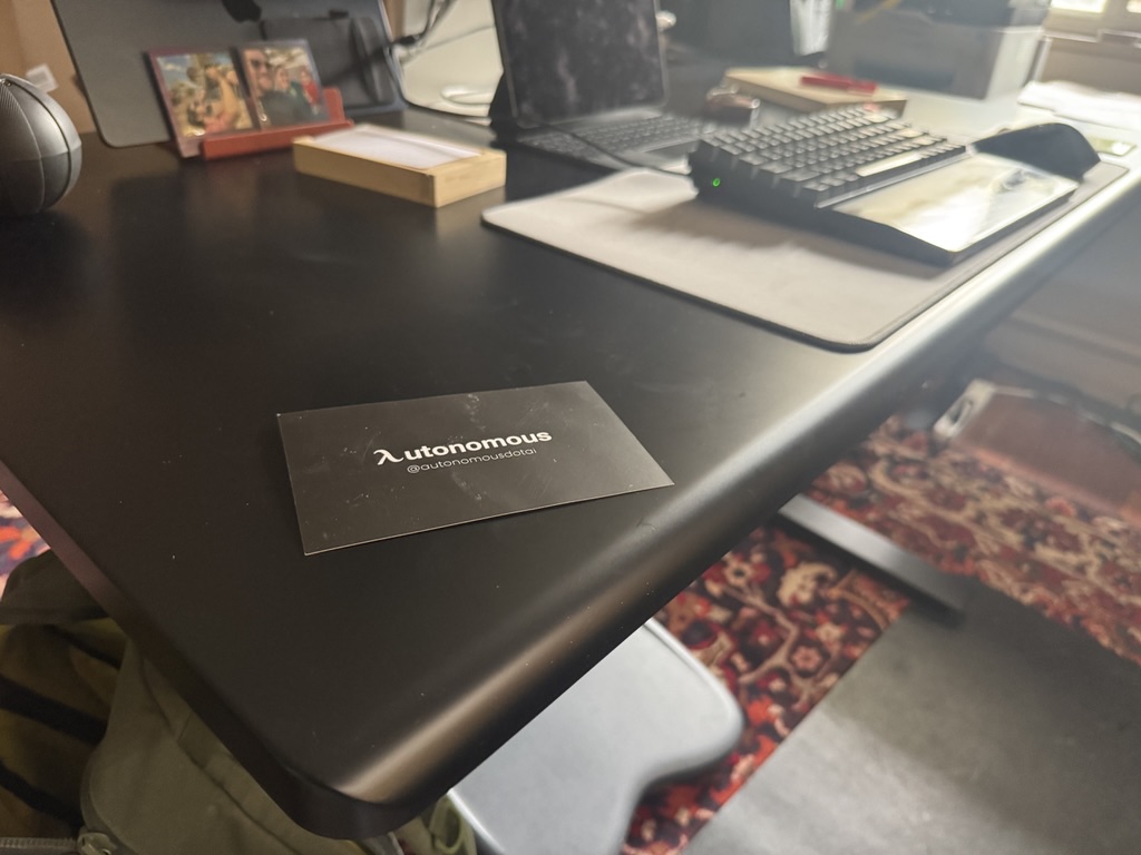 Autonomous branded card on the desk surface showing @autonomousdotai and curved edge detail
