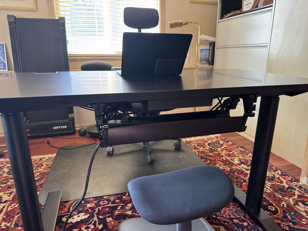 Under-desk cable management tray with power strip mounted, full office view with chair