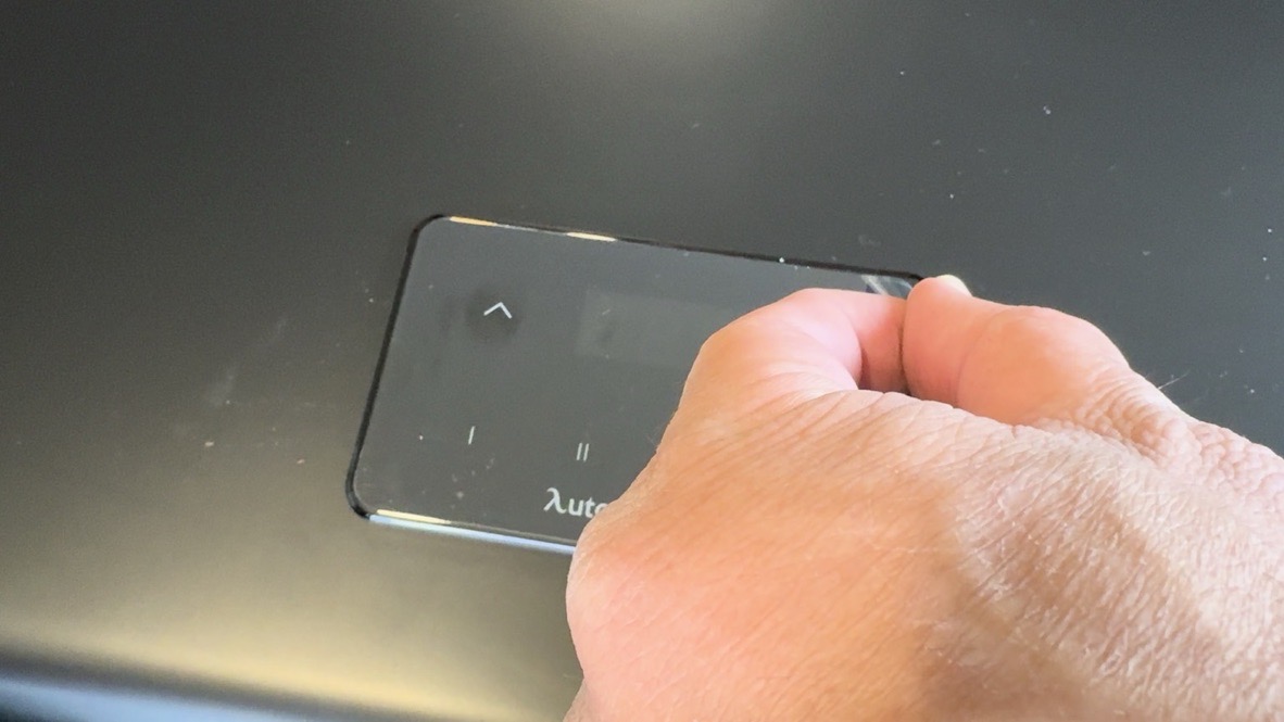 Close-up of hand touching the glass control panel showing up/down arrows, preset buttons I and II, and Autonomous logo