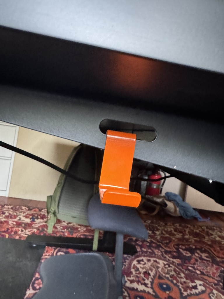 Orange Autonomous headphone hook attached to desk edge via slot, holding a bag strap